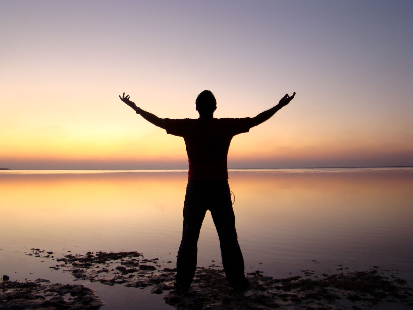 A person standing with arms raised, joyfully greeting the sunrise over the ocean